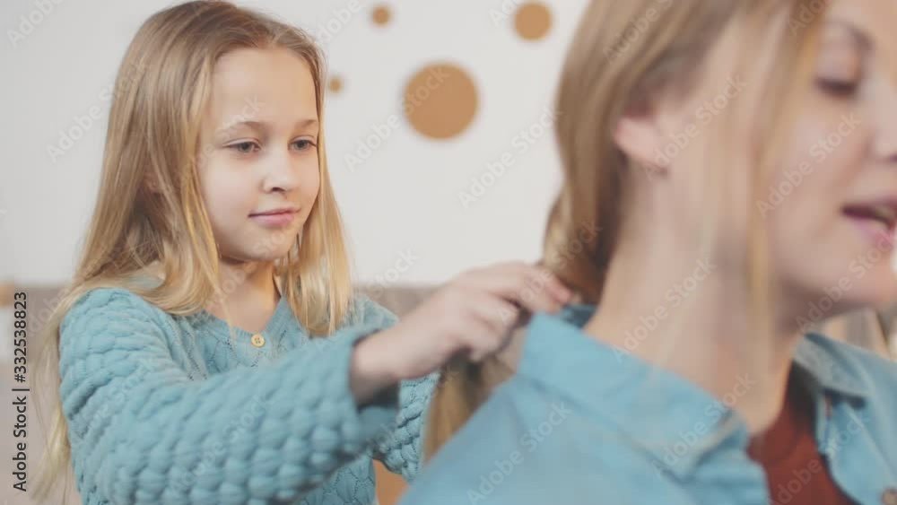Close up of Caucasian cute little girl weaving plait to her mother sitting nearby and talking to her Close up of Caucasian cute little girl weaving plait to her mother sitting nearby and talking to her