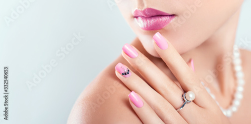 Nail art and design. Beautiful woman wearing make-up and pearl jewellery showing pink manicure with gems. Banner photo