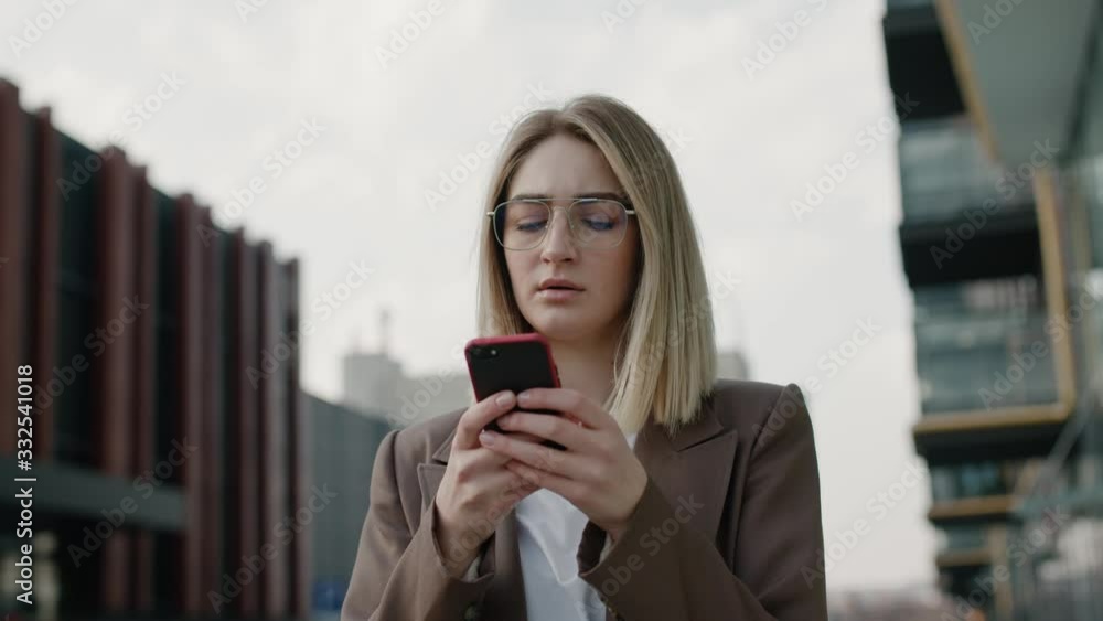 Portrait pretty young businesswoman using smartphone at street Serious woman typing message on smartphone outdoor. European girl holding mobile phone in hand outdoor. Business woman chatting online Portrait pretty young businesswoman using smartphone at street Serious woman typing message on smartphone outdoor. European girl holding mobile phone in hand outdoor. Business woman chatting online
