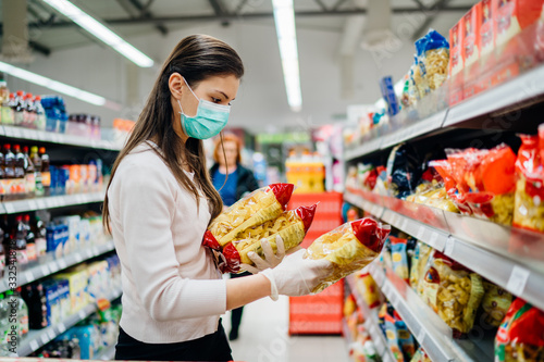 Buyer wearing a protective mask.Shopping during the pandemic quarantine.Nonperishable smart purchased household pantry groceries preparation.Woman buying few pasta packages.Budget pastas and noodles. photo