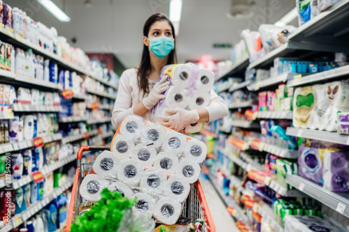 Toilette paper shortage.Woman with hygienic mask shopping for toilette paper supplies due to panic buying and product hoarding during virus epidemic outbreak.Hygiene products deficiency photo