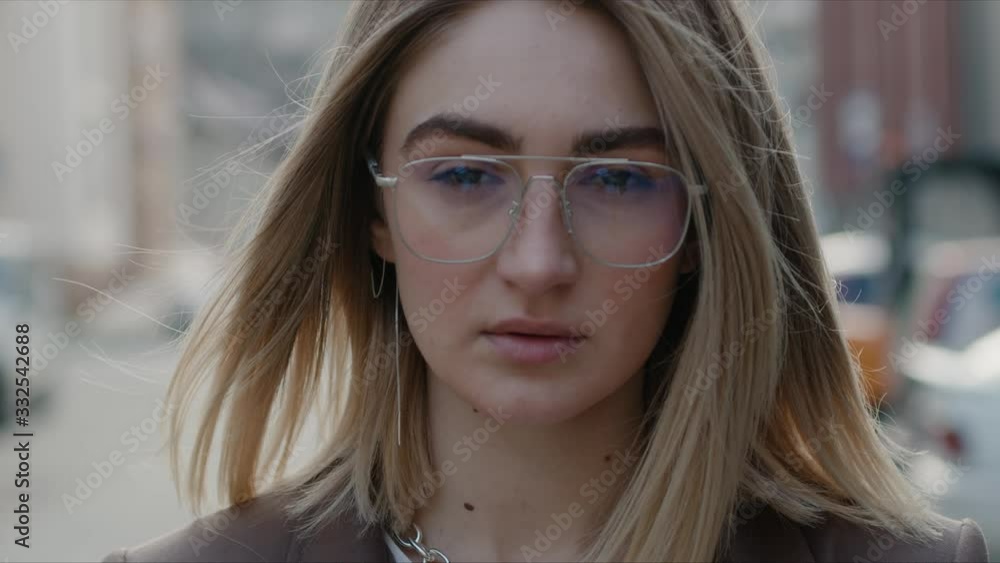 Close up portrait of beautiful and confident young stylish caucasian woman in formal suit and glasses standing outdoors looking at camera wind blowing her hair spring dreamy female slow motion Close up portrait of beautiful and confident young stylish caucasian woman in formal suit and glasses standing outdoors looking at camera wind blowing her hair spring dreamy female slow motion