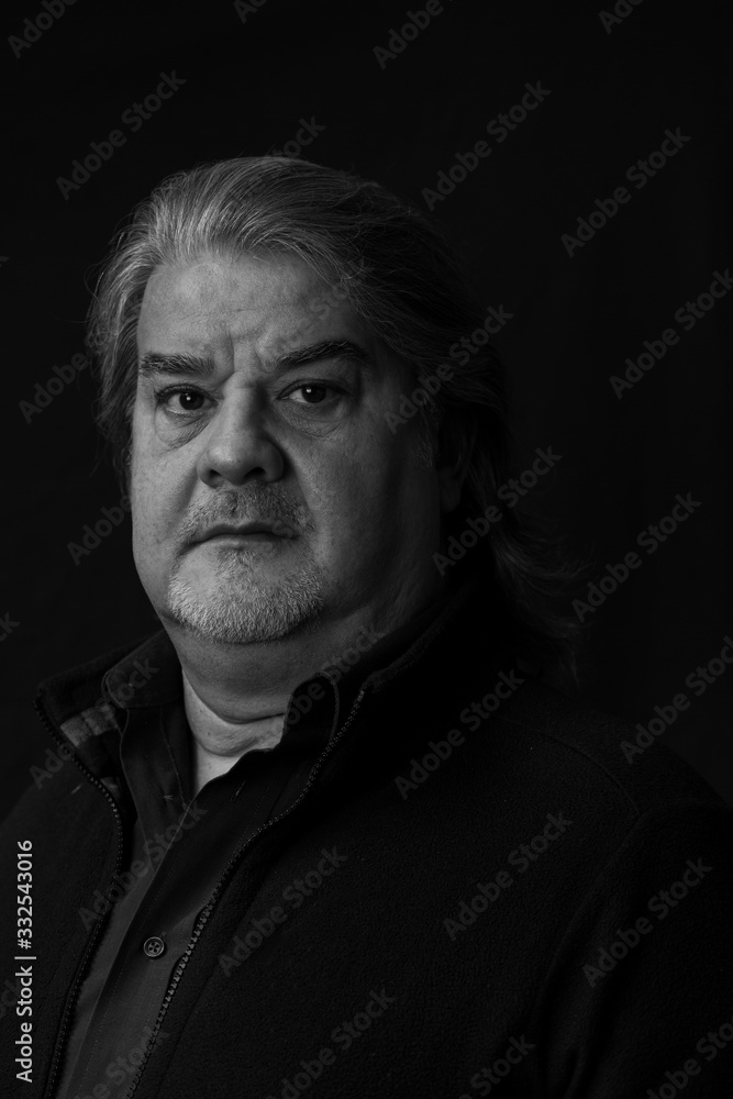 Studio head shot of man. He is serious and looking to the camera. This is a black and white image.