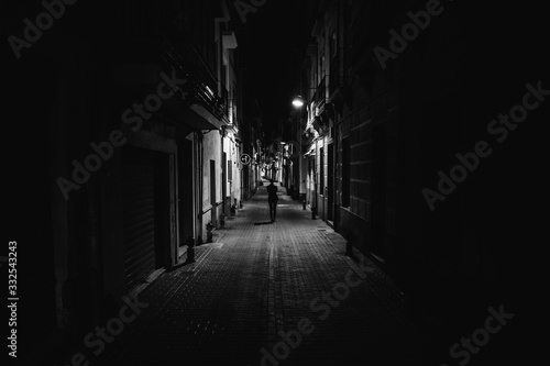 Woman walking alone in the street late at night.Narrow dark alley,unsafe female silhouette.Empty streets.Woman pedestrian alone.Police hour.Assault situation,violence against women concept.