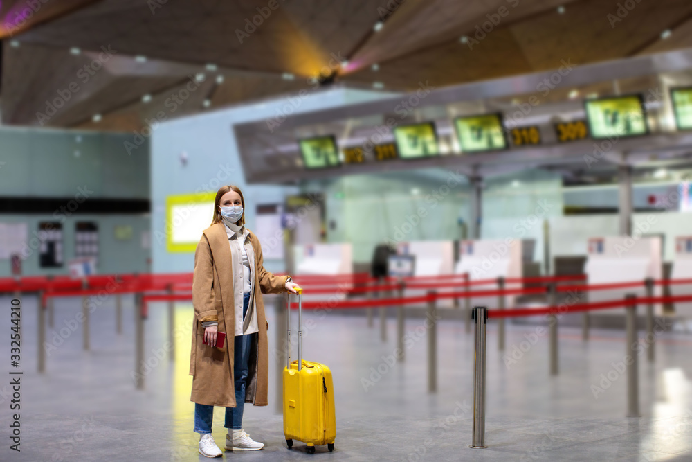 Naklejka premium Woman with luggage stands at almost empty check-in counters at the airport terminal due to coronavirus pandemic/Covid-19 outbreak travel restrictions. Flight cancellation.Quarantine all over the world