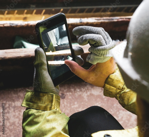 Architect holding a smartphone on construction site. young construction worker is using mobile phone on site. Construction worker with building plans and cellphone. Focus on mobile. warm vivid filter.