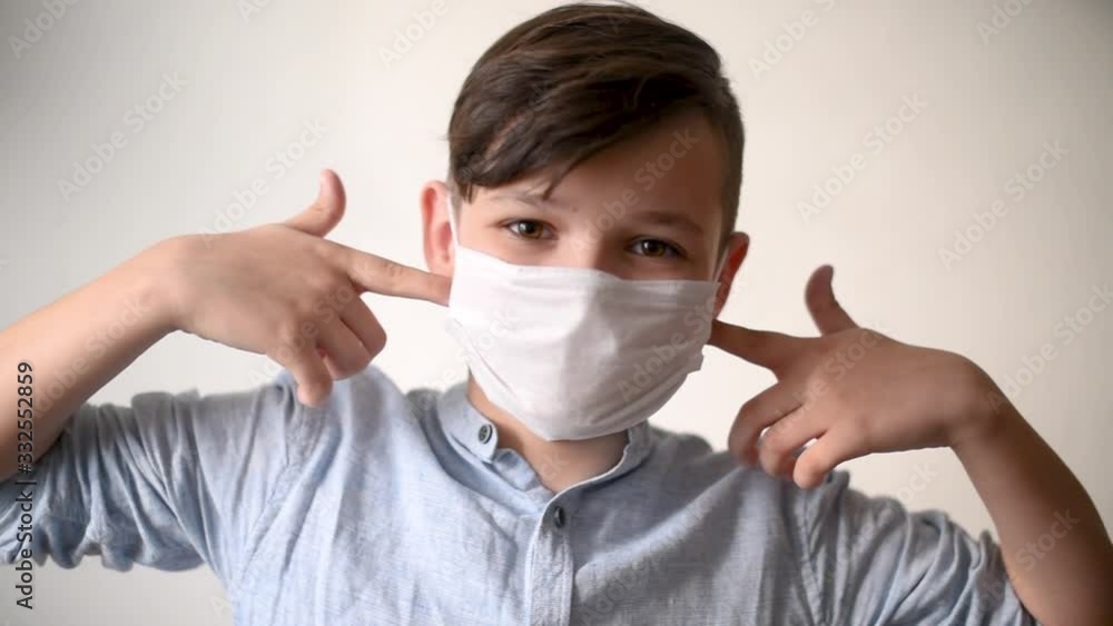 Handsome brunette boy pointing a fingers at the surgical mask on his face. Think about safe follow quarantine rules Handsome brunette boy pointing a fingers at the surgical mask on his face. Think about safe follow quarantine rules