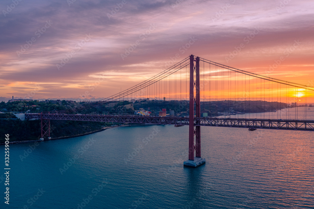 Obraz premium Lisbon, Portugal. Aerial view of the 25 de Abril Bridge (Ponte 25 de Abril, 25th of April Bridge) at sunset. It is often compared to the Golden Gate Bridge in San Francisco, US.