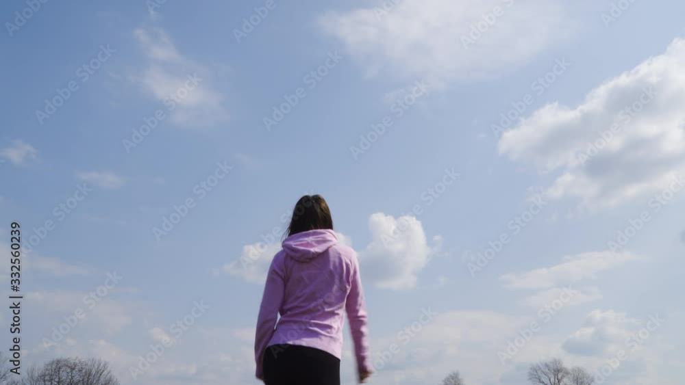 Young caucasian woman is walking on the field, wearing workout clothing, cold weather with wind, tracking low angle shot. Young caucasian woman is walking on the field, wearing workout clothing, cold weather with wind, tracking low angle shot.