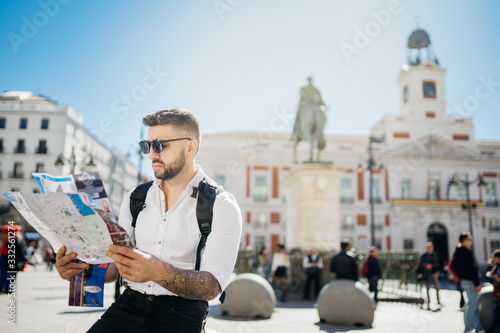 Attractive smiling young man influencer.Tourist visiting famous landmarks and places.Cheerful male traveler at famous Puerta del Sol square,site seeing attractions.Vacation in Spain, blogger lifestyle