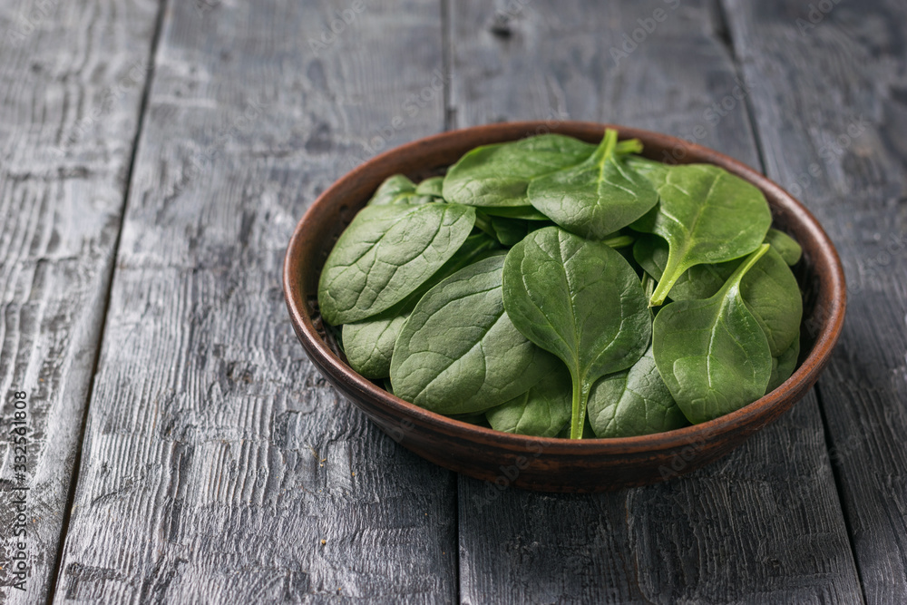 A shallow clay plate with spinach leaves on a wooden table. Food for fitness. A shallow clay plate with spinach leaves on a wooden table. Food for fitness.