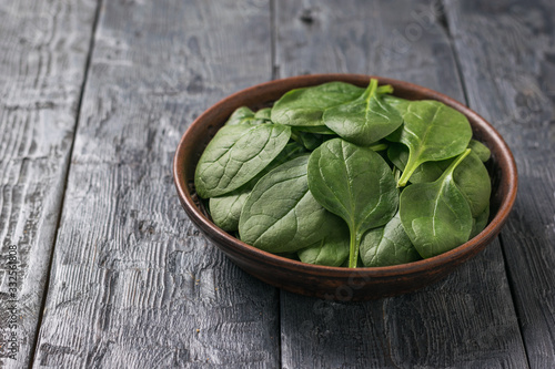 A shallow clay plate with spinach leaves on a wooden table. Food for fitness.
