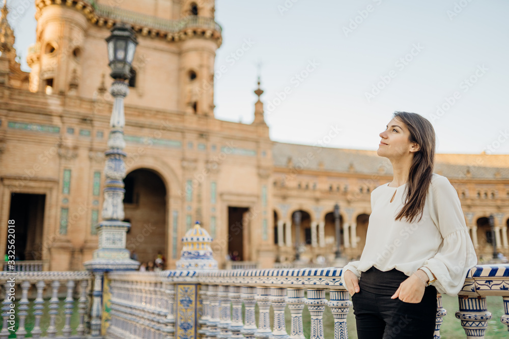 Enjoying beautiful historical landmark.Young tourist woman looking over Plaza de Espana in Seville,Andalusia,Spain.Traveling to Spain.Sunset on Spain Square.Pensive woman in public square in Europe.