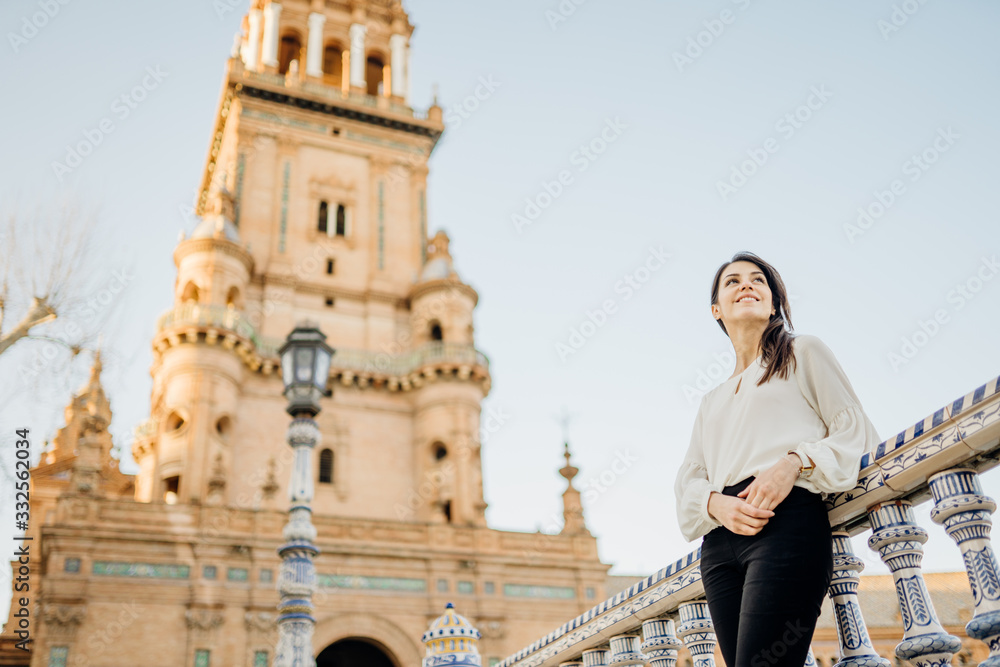 Smiling young tourist woman looking over Plaza de Espana  in, Seville (Sevilla), Andalusia, Spain.Traveling to Spain.Sunset on Spain Square.Female  traveler visiting Spain,enjoying view,mindful walk.
