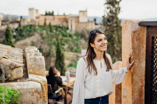 Young tourist woman visiting Granada,Andalucia,Spain.Smiling woman sightseeing old historic landmarks with Alhambra in the background.Excited woman traveling  to Andalucia,Spain.