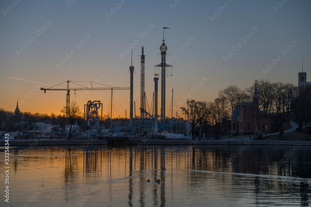 Morning skyline view at sunrise over the district Djurgården with boats, ice and towers in orange back light in Stockholm.