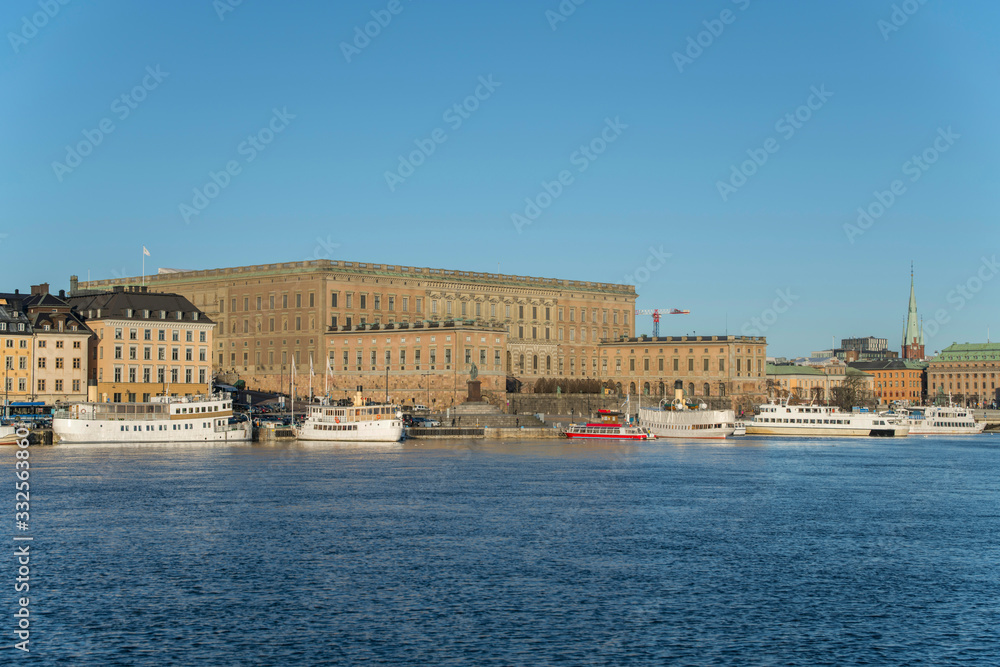 View over the old town district Gamla Stan from the island Skeppsholmen in a sunny spring morning with boats and harbor piers.