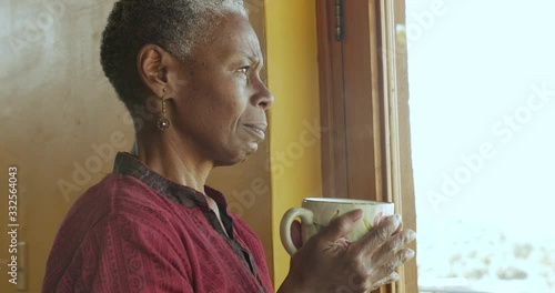 Concerned worried black woman holding a hot coffee cup looking out a window