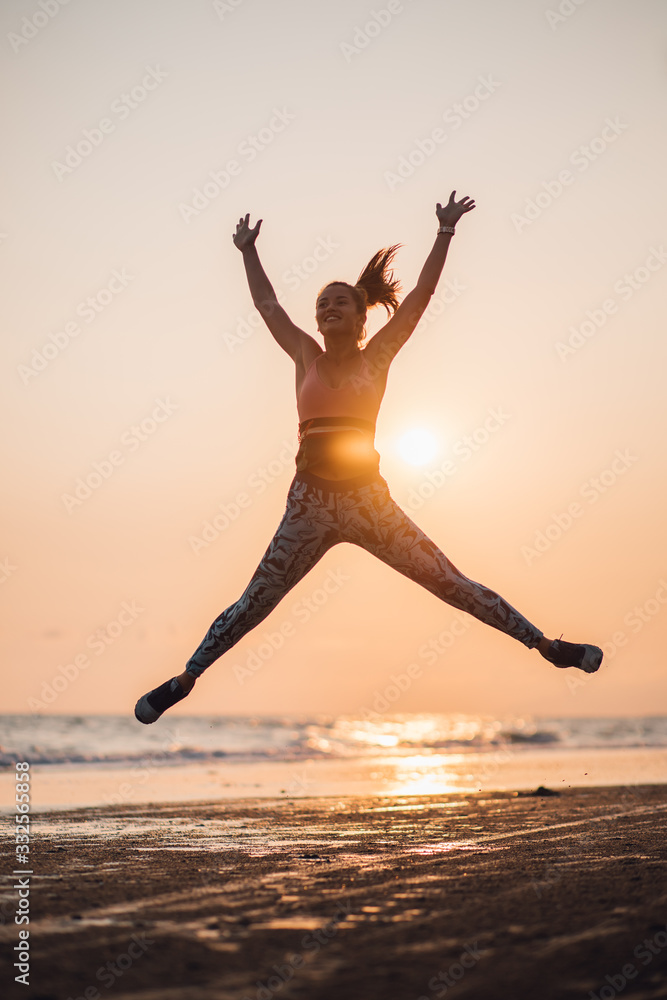 Girl jumping up jogging on the beach in the sunset