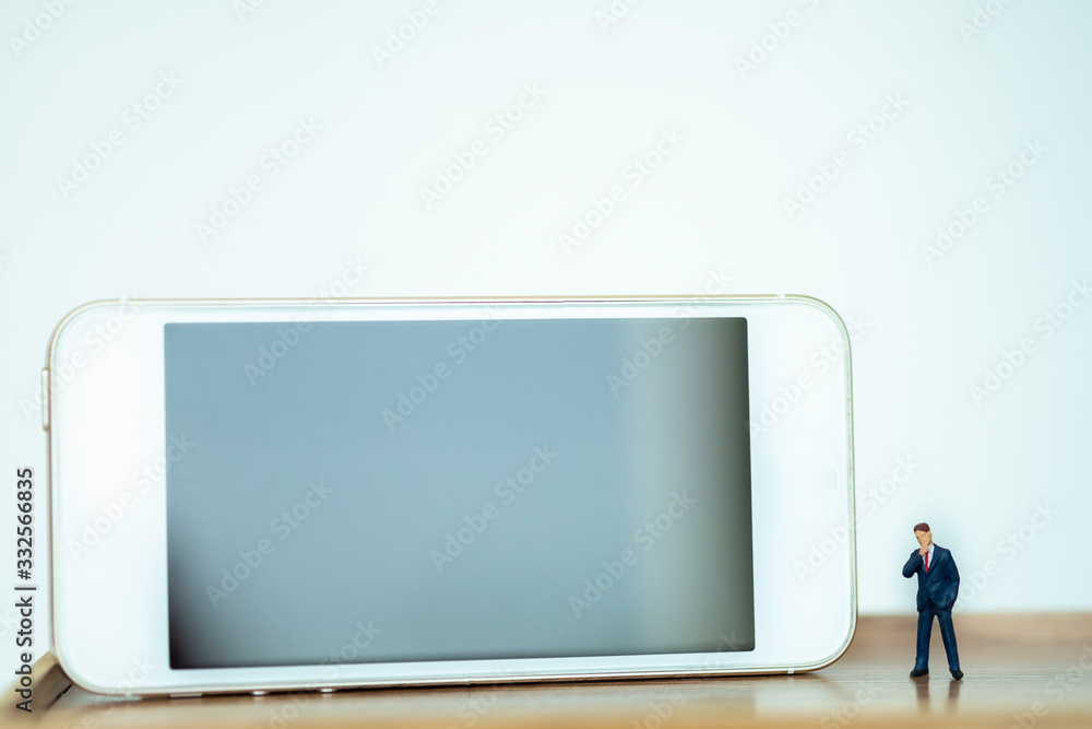 Miniature people: Business man looking Smart phone with copy space for text using as background saving, investment, money, financial, business analytics concept. Miniature people: Business man looking Smart phone with copy space for text using as background saving, investment, money, financial, business analytics concept.