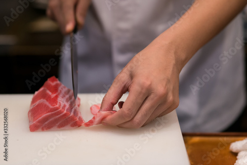 Japanese chef is neatly cutting on fine part of yellow fine tuna to make nigiri maguro sushi