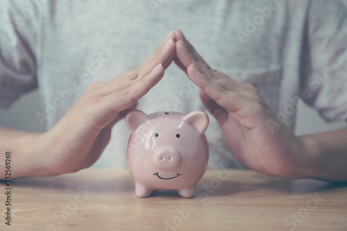 Man hand protect piggy bank on wood table. Save money and financial investment