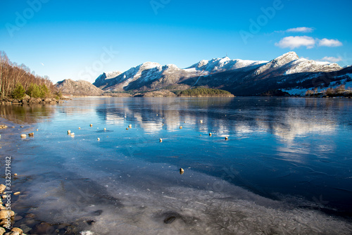 Rocks on top of ice crust of the frozen Oltedalsvatnet lake and scenic landscape of mountains, Gjesdal commune, Norway, February 2018