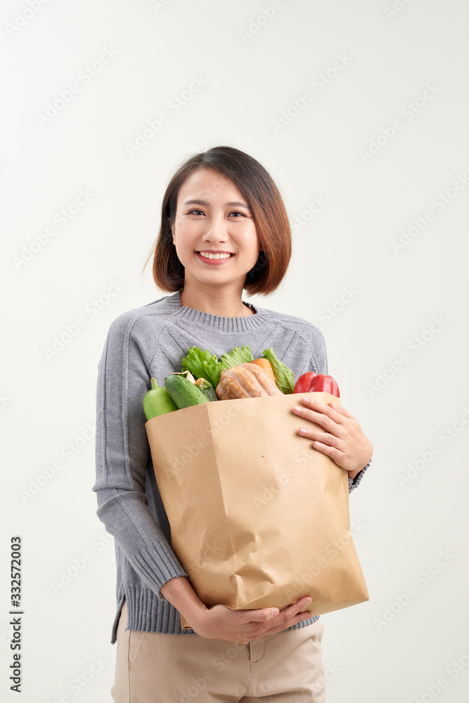 Beautiful young woman in apron holding paper shopping bag full of fresh vegetables and smiling Beautiful young woman in apron holding paper shopping bag full of fresh vegetables and smiling