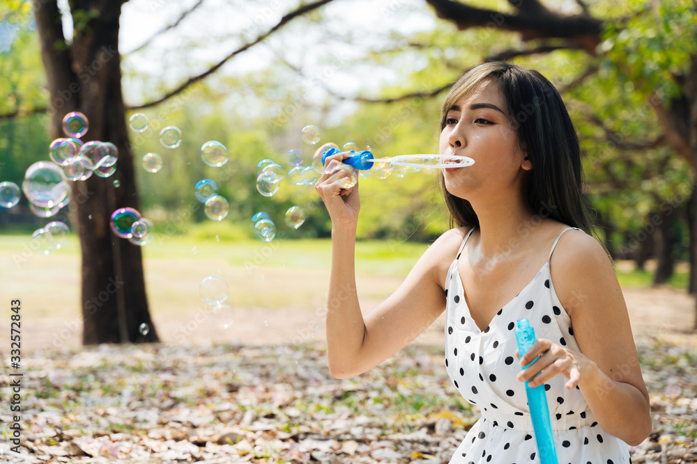 South East Asian ethnic 20s woman blowing air bubbles in the park Young Happy girl wears stylish dress with trees in background. Outdoor summer weekend activity - with copy space South East Asian ethnic 20s woman blowing air bubbles in the park Young Happy girl wears stylish dress with trees in background. Outdoor summer weekend activity - with copy space