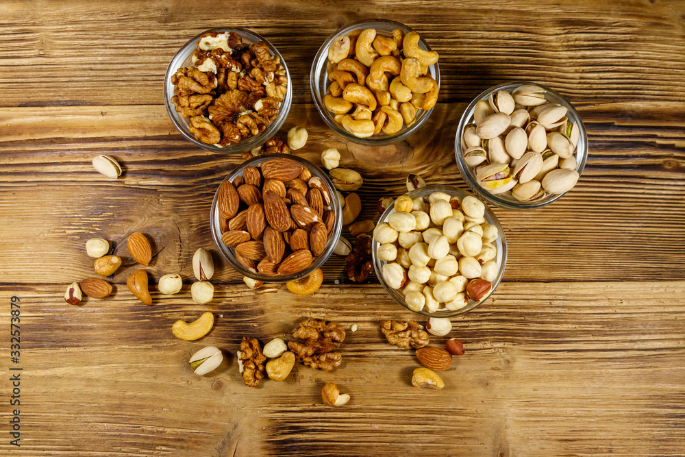 Assortment of nuts on wooden table. Almond, hazelnut, pistachio, walnut and cashew in glass bowls. Top view. Healthy eating concept Assortment of nuts on wooden table. Almond, hazelnut, pistachio, walnut and cashew in glass bowls. Top view. Healthy eating concept