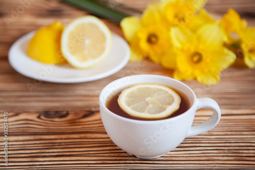 Cap of tea with lemon and flowers on the wooden table.