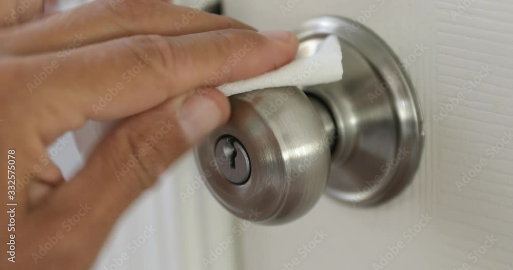 A man sanitizes a doorknob with a disinfectant wipe before entering. A man sanitizes a doorknob with a disinfectant wipe before entering.