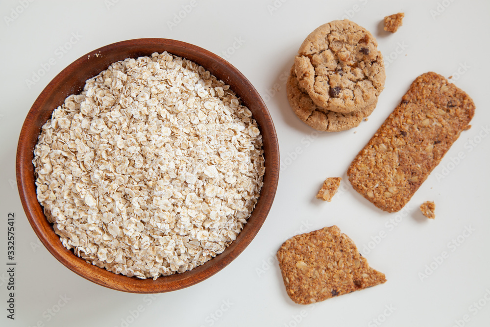 Dry oatmeal in a round wooden plate and oatmeal cookies on the table. Dry oatmeal in a round wooden plate and oatmeal cookies on the table.
