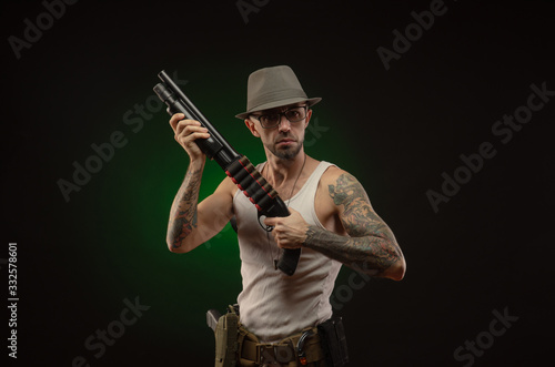 athletic guy with a tattoo poses with a shotgun