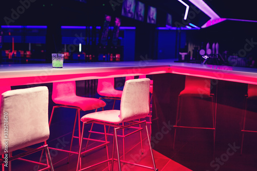 Sticker Glass of bright green neon cocktail on a bar table in night club blue and red lights