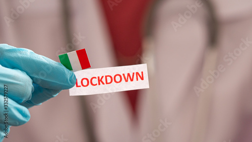 The doctor wears blue gloves holding note paper have text "Lockdown" and Italian flag. Concept Lockdown covid-19.