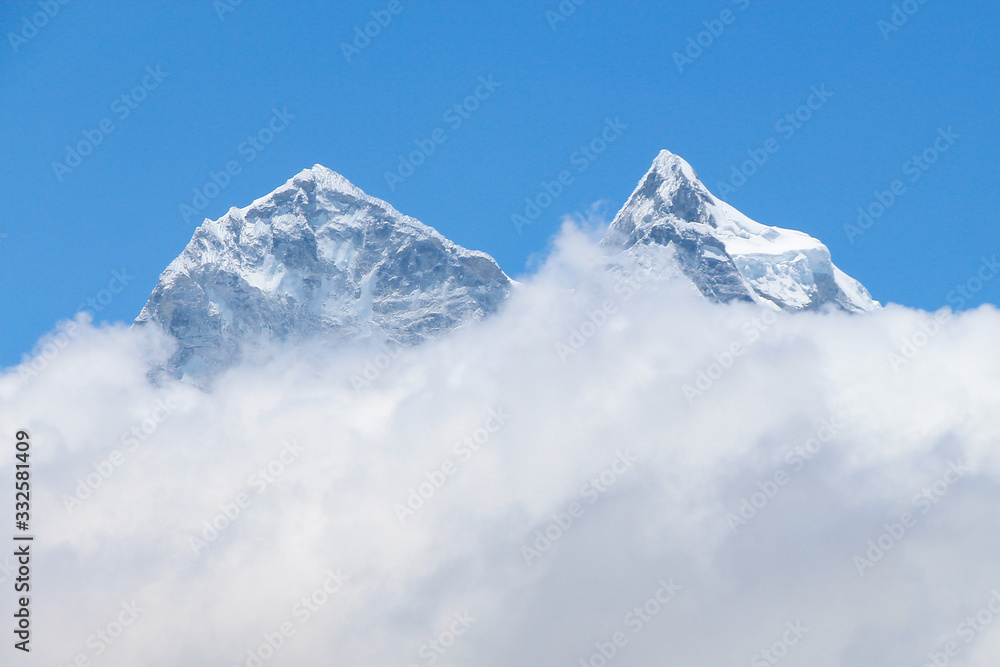 View of white snowy Kangtega mountain peak above clouds in Himalayas during the day on the way to Everest base camp in Nepal. Clear blue sky. Theme of beautiful mountain landscapes.