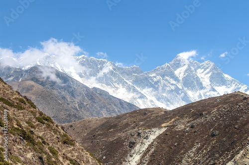 Everest and Lhotse mountain peaks rises above mountain valley in Himalayas during the day on the way to Everest base camp in Nepal. Clouds on mountainside. Theme of beautiful mountain landscapes.