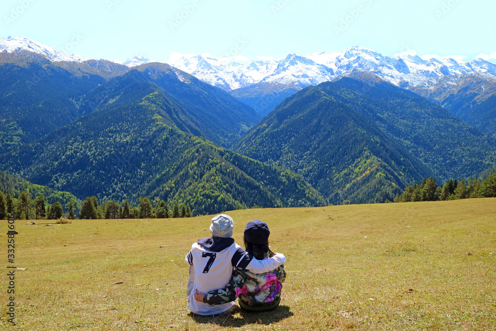 Couple Enjoy the Incredible View of Snow Capped Caucasus Mountain from the Highland in Mestia, Svaneti Region of Georgia Couple Enjoy the Incredible View of Snow Capped Caucasus Mountain from the Highland in Mestia, Svaneti Region of Georgia