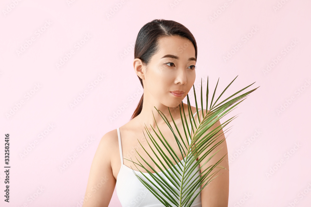 Beautiful young Asian woman with tropical leaf on color background Beautiful young Asian woman with tropical leaf on color background
