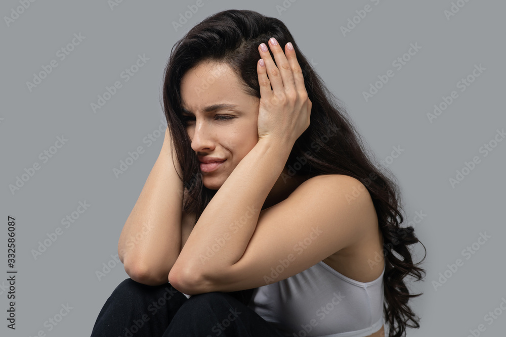 Beautiful dark-haired girl in a white top holding her head and feeling stressed Beautiful dark-haired girl in a white top holding her head and feeling stressed