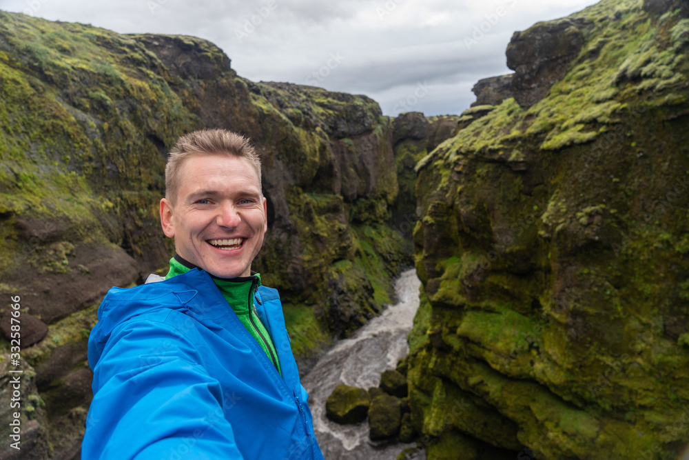 Naklejka premium Young smiling man with river and green canyon on background takes a Selfie. Concept of freedom movement and freedom