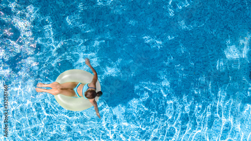 Active young girl in swimming pool aerial top view from above  child relaxes and swims on inflatable ring donut and has fun in water on family vacation  tropical holiday resort