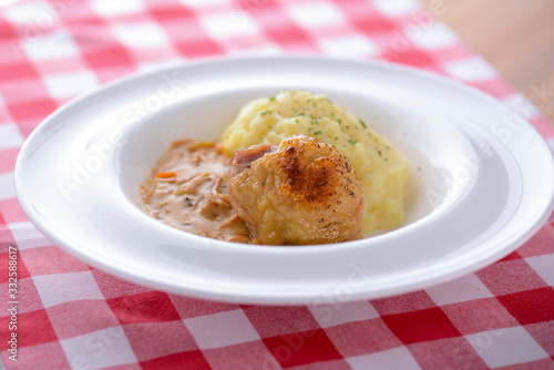 Traditional cuisine, mashed potatoes with gravy, meat and dill served on a white plate on a plaid background