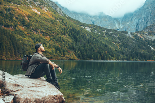 man sitting on the rock in front of lake in mountains enjoying the view