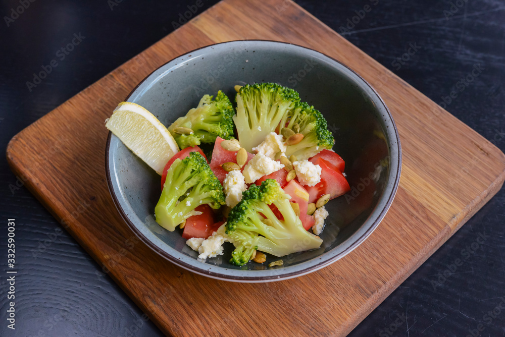 One plate of vegetable salad with feta cheese, cucumbers, tomatoes, and broccoli served in bowl on rustic wooden board. One plate of vegetable salad with feta cheese, cucumbers, tomatoes, and broccoli served in bowl on rustic wooden board.