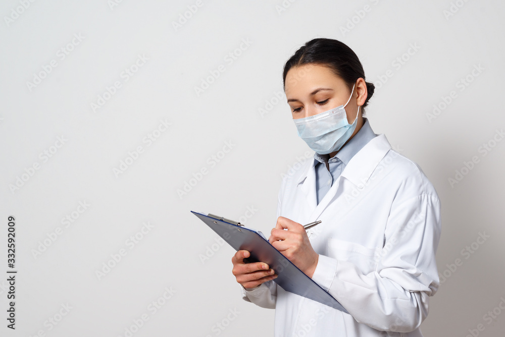 portrait of a female doctor in a protective mask with a clipboard and a pen in her hands, making a record. portrait of a female doctor in a protective mask with a clipboard and a pen in her hands, making a record.
