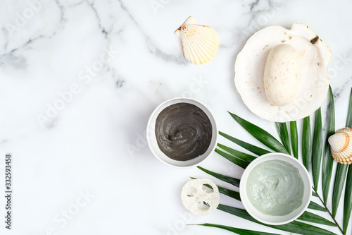 SPA natural organic cosmetic clay mask and powder in bowls and tropical palm leaf on marble table. Beauty products for face skin care and treatment concept.