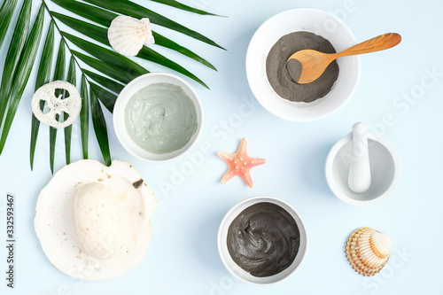 SPA natural organic beauty products for face skin care and treatment. Cosmetic clay mask and powder in bowls, homemade soap and tropical palm leaf on pastel blue background. Top view, flat lay.