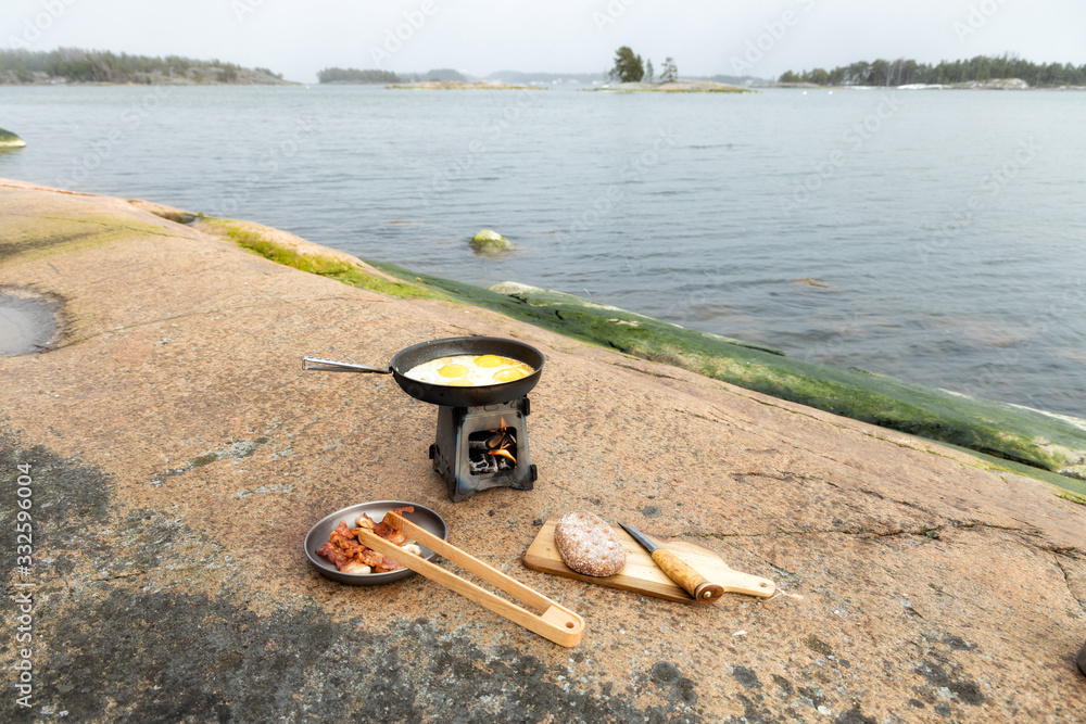 Cooking breakfast on a wood burning camp stove on the rock near the sea. Travel, adventure, camping gear, outdoors items.